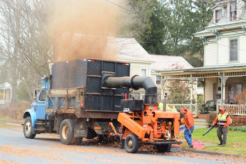 Workers collect autumn leaves with machinery on a residential street in Cambridge, NY.